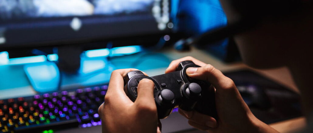 Photo closeup of asian gamer boy playing video games online on computer in dark room, wearing headphones with microphone and using joystick